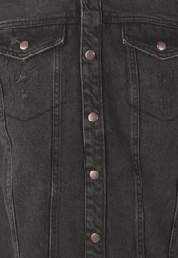 Chaqueta de mezclilla negra con botones de presión de metal, dos bolsillos en el pecho, detalles desgastados y un diseño estructurado con costuras visibles.