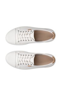 Coppia di sneakers basse in pelle bianca con lacci, tallone color cuoio e etichetta con marchio sul lato, viste dall'alto su sfondo bianco.