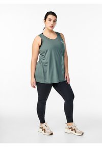 Grünes sportliches Tanktop, lockere Passform, mit rundem Ausschnitt. Schwarze Leggings, enganliegend. Beigefarbene Sneakers mit braunen Akzenten.