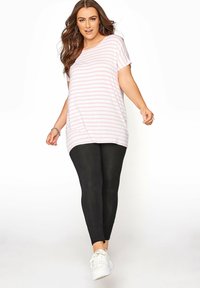 Ljusrosa och vita randiga oversize T-shirt som kombineras med svarta leggings och vita sneakers. T-shirten har korta ärmar och en rundad nederkant.