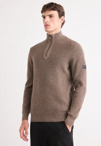 Barna kötött pulóver, félig cipzárral ellátott gallérral, amely texturált anyagból készült, slim fit fazonú és logóval ellátott a bal ujján.
