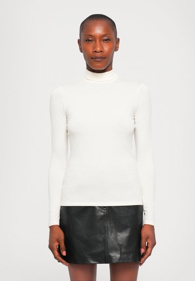 Chemisier blanc à manches longues et col roulé, en tissu doux, associé à une jupe mini en cuir noir, mettant en valeur un design ajusté et une texture lisse.