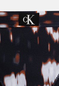 Svart stoff med et abstrakt mønster i oransje og hvitt; har et svart rektangulært merke med "cK"-logo; glatt tekstur.