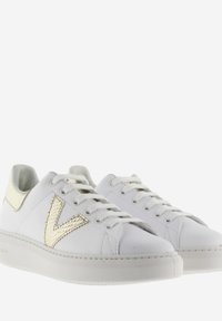 Baskets en cuir blanc avec des accents dorés, arborant un logo 'V' texturé, un bout arrondi et un système de laçage. Semelle en caoutchouc pour une meilleure adhérence.