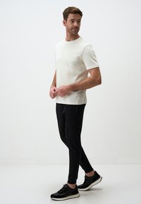 Beige Kurzarmhemd kombiniert mit schwarzen schmalen Hosen und schwarzen Sportschuhen. Glatte Stofftextur und schlichtes Design.