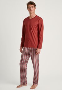 Chemise rouge à manches longues avec poche, associée à un pantalon de pyjama à carreaux rouge, blanc et bleu. Tissu doux, coupe décontractée, design minimal.