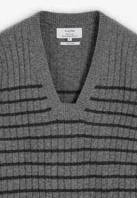 Grå stickad tröja med V-ringning, med ribbad textur och mörka horisontella ränder. Etiketten anger storlek S och ett speciellt garnmaterial.