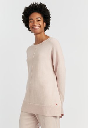 Pull en tricot rose clair avec une coupe décontractée, encolure ronde et poignets côtelés. Présente une couture centrale et un petit logo rouge sur l'ourlet.