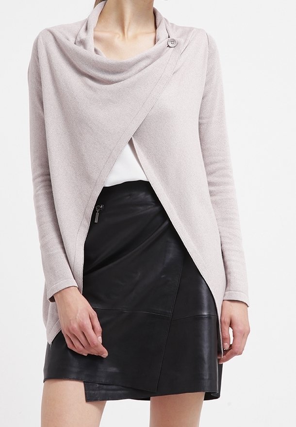 Helle rosa, drapierte Strickjacke mit einem einzigen Knopfverschluss, aus weichem Material; kombiniert mit einem schwarzen Lederrock mit asymmetrischem Saum.