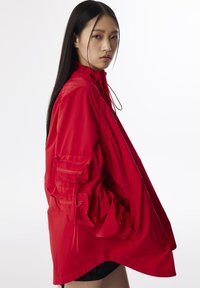 Rode lichtgewicht jas met een hoge kraag, elastische manchetten en twee ritszakken aan de zijkant. Heeft een losse, oversized pasvorm met geplooide details.