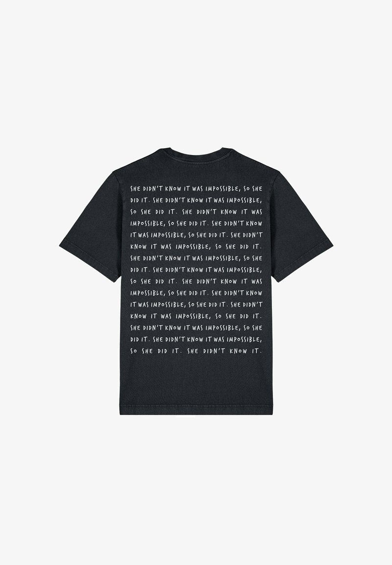 T-shirt en coton noir à manches courtes. Texte imprimé en blanc au dos, répétant une phrase sur le dépassement de l'impossible. Encolure arrondie.