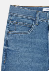 Vaqueros de denim azul con un corte clásico, con costuras anaranjadas, un bolsillo frontal y una etiqueta en la cinta de la cintura. La tela tiene una textura suave.