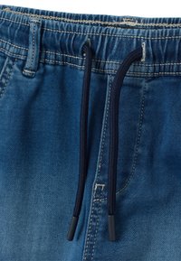 Pantalones cortos de mezclilla con cintura elástica, color azul degradado, con cordones de color azul oscuro con puntas de plástico. Costuras visibles alrededor de la cintura.