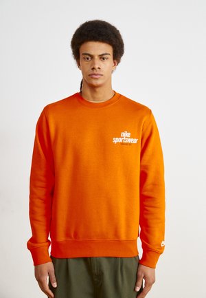 Sweatshirt laranja feito de uma mistura de algodão, com gola redonda, punhos canelados e um logótipo branco da Nike Sportswear no lado esquerdo do peito.