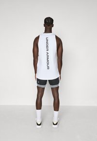Balta be rankovių marškinėliai su „UNDER ARMOUR“ užrašytu juodu spalva nugaroje, derinami su pilkais tinkliniais šortais ir baltais puskojiniais.
