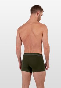 Boxer shorts de algodón verde con una cinturilla elástica de marca, llevados al revés, con una textura suave y un diseño ajustado.