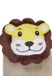 Beige gestrickte Socke mit einem plüschigen Löwenkopf-Akzent. Das Gesicht des Löwen ist gelb mit schwarzen Augen, rosa Wangen und einer braunen Mähne.