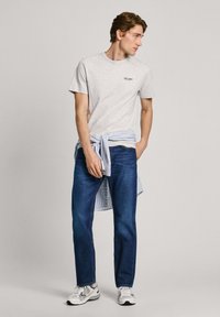 Gaiši pelēks T-krekls ar "Pepe Jeans" logo, tumši zilas džinsus un svītrainu krekliņu, kas sasiets ap vidu. Balti sporta apavi noslēdz šo izskatu.