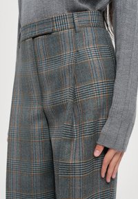 Harmaa ruudullinen housut, jotka on valmistettu villasekoitteesta ja joissa on sekoitus sinisiä, oransseja ja mustia viivoja. Muotonsa mukaisesti leikattu, sivutaskut ja vyölenkit.