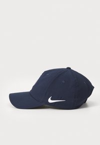 Tamsiai mėlyna beisbolo kepuraitė, pagaminta iš audinio, su išlenktu kraštu, tamsiomis siūlėmis ir baltu Nike logotipu priekyje.