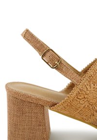 Beige geweven sandaal met hoge hak en vierkante blokhak, verstelbare band met gouden gesp en textuurdetails.