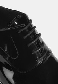 Schwarzer Lacklederschuh mit glatter, glänzender Oberfläche, traditioneller Schnürung und abgerundetem Zehendesign. Akzente setzen kontrastierende Nähte.