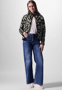 Schwarz-weiß bedruckte Bomberjacke mit hohem Kragen, kombiniert mit hochtaillierten blauen weiten Jeans und hellen Sneakers.