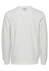 Sudadera blanca de cuello redondo hecha de algodón suave, con mangas largas, puños y dobladillo acanalados, y una pequeña etiqueta impresa en la parte posterior del cuello.