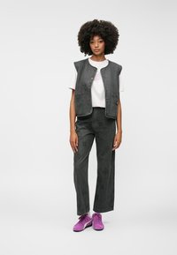 Grå denimvest med lommer, paret med matchende grå vide bukser med et subtilt mønster, og lyse lilla sneakers.