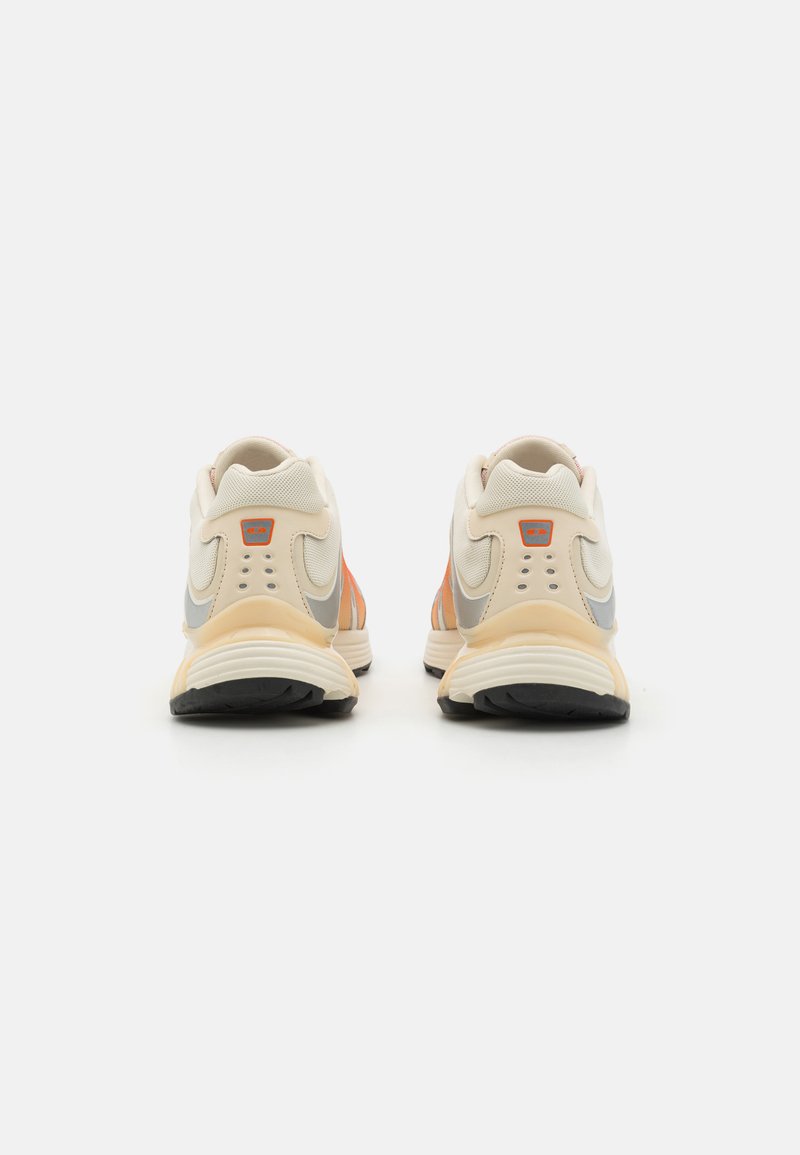 Zapatillas con una parte superior de color beige claro, acentos en naranja y gris, y una sección de malla texturizada. Cuenta con una suela gruesa y un diseño detallado en el talón.