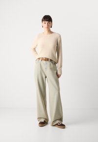 Beige textúrájú pulóver, világoskék, bőszárú farmernadrág, barna öv kerek csattal és barna/krém színű tornacipők. Egyszerű dizájn, puha anyagok.