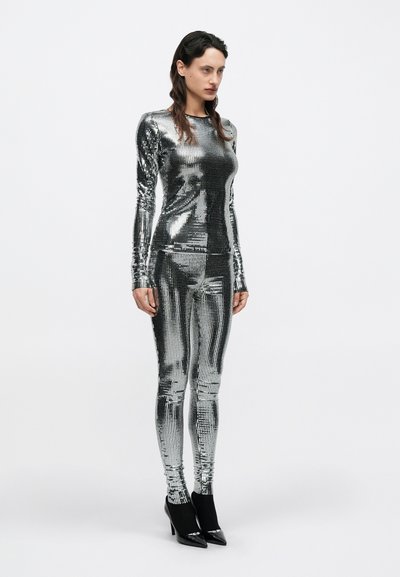 Metallist hõbedane kokkupressiv ülikond, millel on pikad varrukad ja sobivad retuusid. Sile, peegeldav tekstuur ning keha vormi järgiv lõige. Mustad kontsakingad.