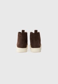 Brown suede high-top sneakers with a white rubber sole, featuring a loop at the back for easy wear and minimal stitching detail.