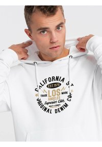 Sudadera blanca hecha de una tela suave que presenta un estampado gráfico circular con texto y acentos en negro y dorado. Cuerdas en la capucha.