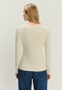 Top a maniche lunghe in maglia a coste di un beige chiaro, con scollatura rotonda e vestibilità aderente. Abbinato a jeans in denim blu.