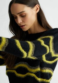 Maglione nero con strisce ondulate gialle e accenti metallici, caratterizzato da un filato morbido e testurizzato e un'ampia scollatura.