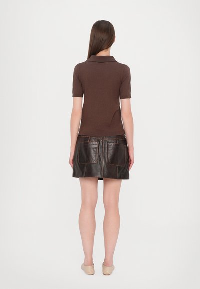 Polo marron à manches courtes, associé à une jupe en cuir noire avec deux poches avant et des détails de couture marron.