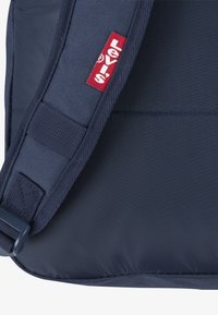 Granatowa torba na ramię z płótna o fakturowanej tkaninie, z czerwoną naszywką logo Levi's i regulowanym paskiem zapewniającym bezpieczne noszenie.