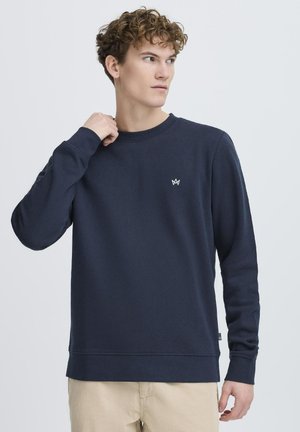Navy blue sweatshirt made of cotton blend; features long sleeves, a round neckline, and a small white logo on the chest.