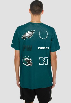Homme portant un t-shirt vert des Philadelphia Eagles avec le logo de l'équipe, un casque, un texte et un symbole de conférence NFL dans le dos.