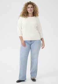 Light cream knitted sweater with three-quarter sleeves paired with light blue straight-leg jeans and black flats. Simple, seamless design.