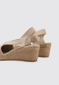 Cuñas de esparto beige con suela de yute trenzado, aberturas acanaladas y parte superior de ante suave. Presentan un tacón bajo y un diseño de espalda abierta.