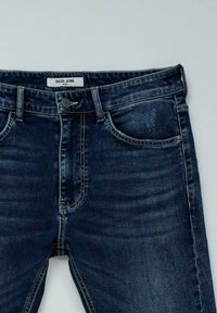 Tamno plave uske traperice od denima s srednje visokim strukom, kontrastnim šavovima i pet džepova. Oznaka "Salsa Jeans" na unutrašnjem pojasu.