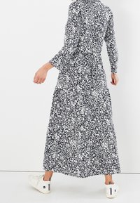 Černobílé květinové maxi šaty s dlouhými rukávy, kulatým výstřihem a vrstvenou sukní. V kombinaci s bílými teniskami s černými akcenty.