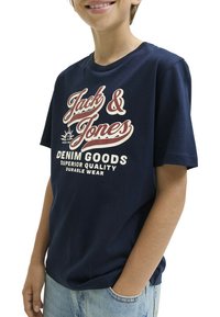 Camiseta de algodón azul marino con estampado retro de logo en blanco y rojo. Manga corta y corte relajado, combinada con pantalones cortos de denim claro.