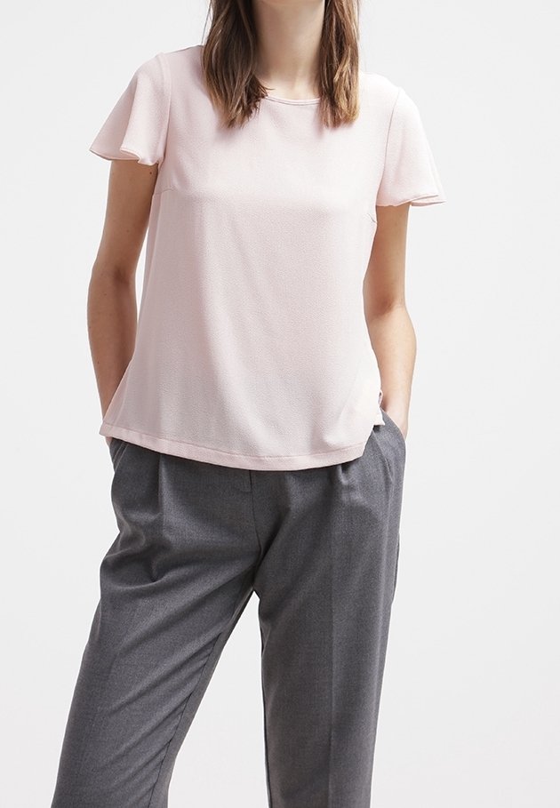Ljusrosa kortärmad blus med en slät textur och subtil lyster. Matchad med lösa grå byxor, vilket ger en avslappnad look.