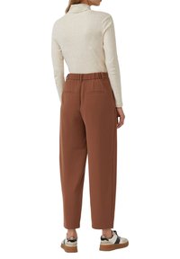 Brązowe spodnie zwężane z elastycznym pasem, dwie tylne kieszenie, w połączeniu z wielokolorowymi trampkami oraz jasnobeżową bluzką z długim rękawem.