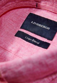 Roze linnenmix stof met een gladde textuur. Twee labels: één zwart met de tekst "LINDBERGH," een ander met "Linnenmix" in witte tekst.