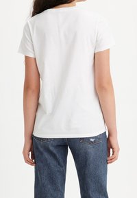 Bílý bavlněný tričko s krátkými rukávy a kulatým výstřihem, pohled zade. V kombinaci s modrými džínami s kapsami na zadní straně.