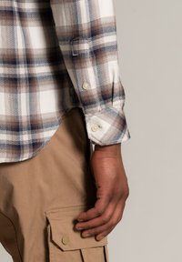 Rutig flanellskjorta med blå, brun och vit mönster. Har knäppning vid ärmsluten och en fiskbensstruktur. Kombinerad med beiga cargobyxor.